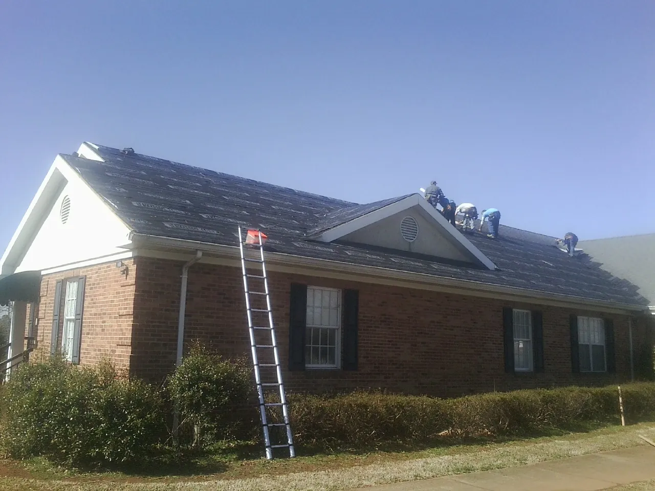 Crew tearing shingles off a brick ranch roof with a ladder set — Metal Roof Repair work by our crew in Joelton