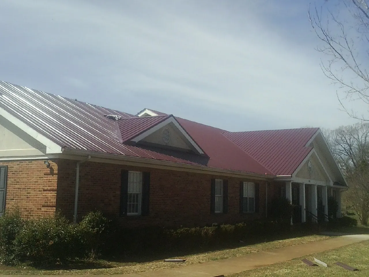 Red metal roof with gabled entries on a long brick building, from a Hail Damage Roof Repair job in Joelton