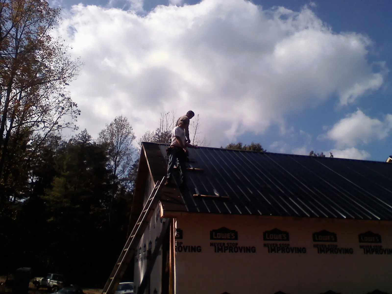 Roofer fastening dark metal panels high against a cloudy sky, from a Roof Inspection job in Joelton