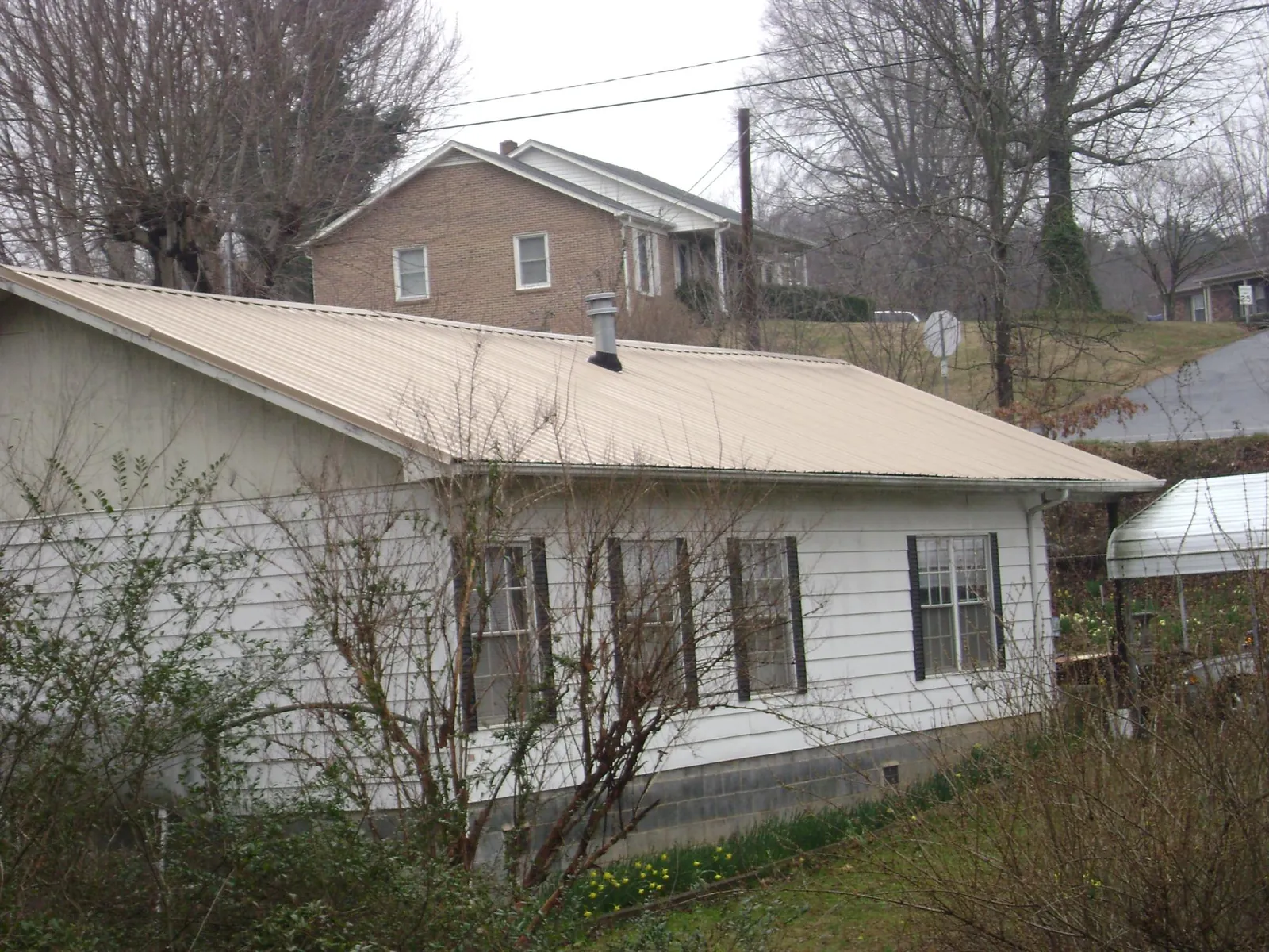 Tan metal roof on a white sided house set into a hillside — Commercial Roofing by Roofing Brothers in Joelton