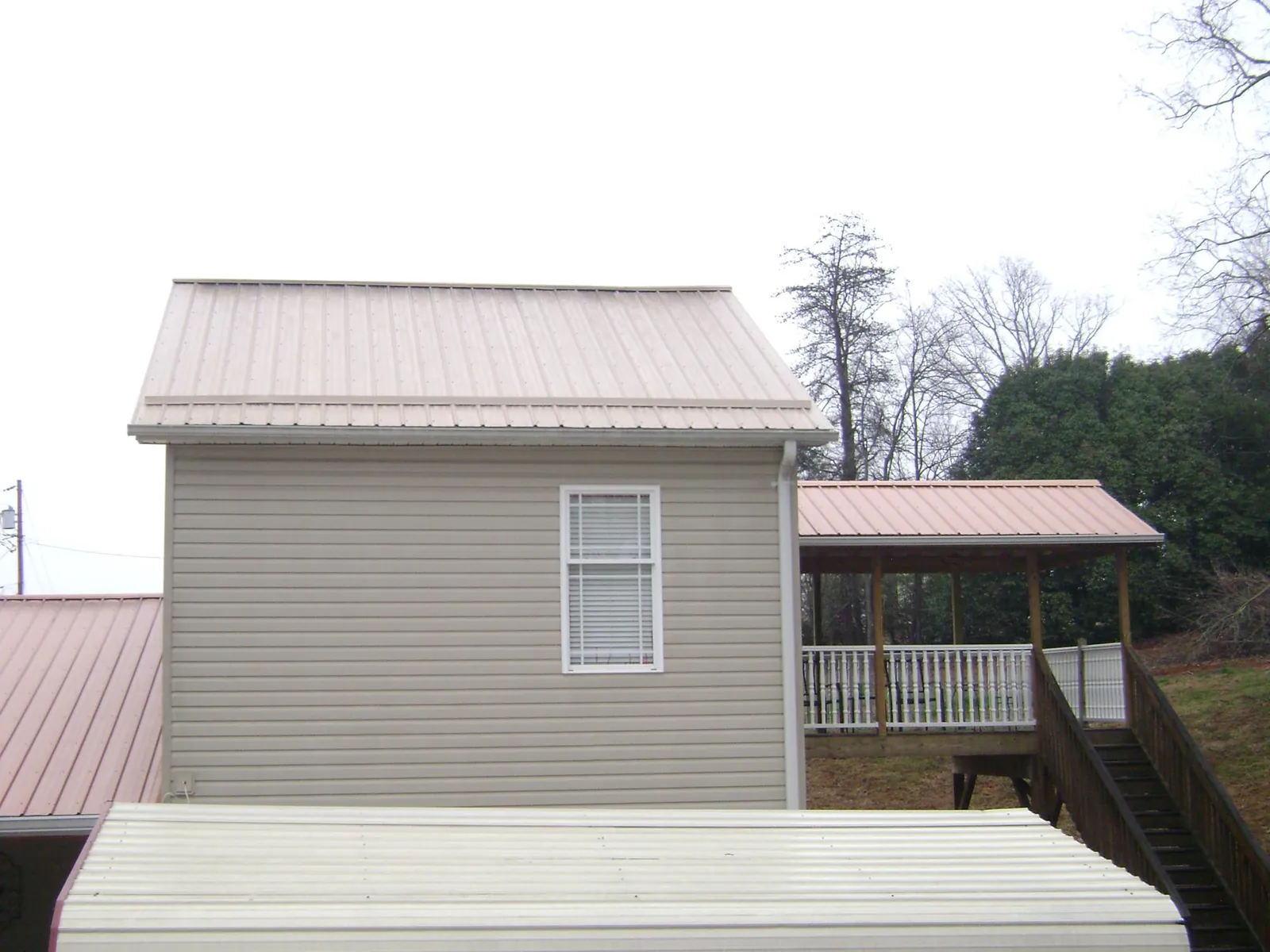 Tan metal roofs on a two story addition and attached porch, from a Roof Replacement job in Joelton